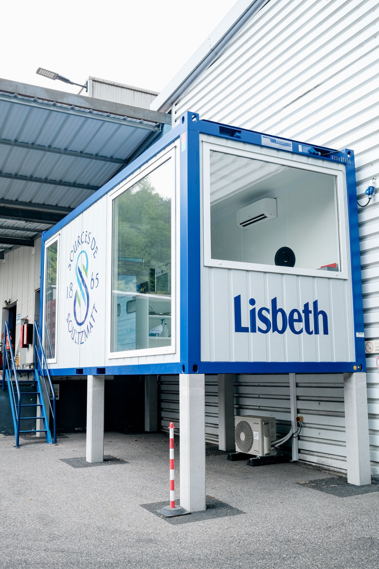 Petit bureau modulaire vitré près d’un bâtiment industriel